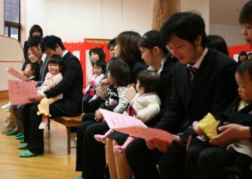 正装をしたお父さんやお母さんとおしゃれをした小さな子ども達が膝の上に抱っこされて、入所者の親子が入所式に臨んでいるわちエンジェル入所式の写真