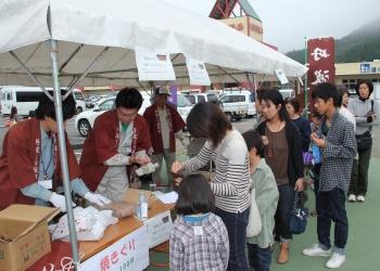 焼きぐりを販売しているテントに行列が出来ており、子ども連れの来場者がえんじ色の法被を着た店主に支払いをしている写真