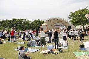 広々とした会場で、来場者がシートを広げており、音楽に合わせて両手を挙げて、ステージを楽しんでいる様子を後方より写した写真