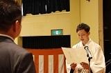 白い羽織袴を着た新成人がスーツを着た男性の前に立って、白い用紙を持って話をしており、新成人の誓いを述べている写真