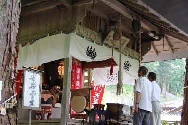建物の周りを白い幕で囲まれている神社で、男性の参拝客2名が拝殿で参拝している写真