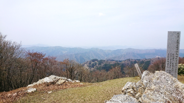 石碑や岩が置いてある山頂から、遠くの山脈を撮影した風景の写真