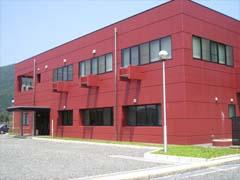 赤い外壁で2階建て、四角い窓が5個ずつ並んでいる京丹波町水道事業畑川浄水場の建物の写真